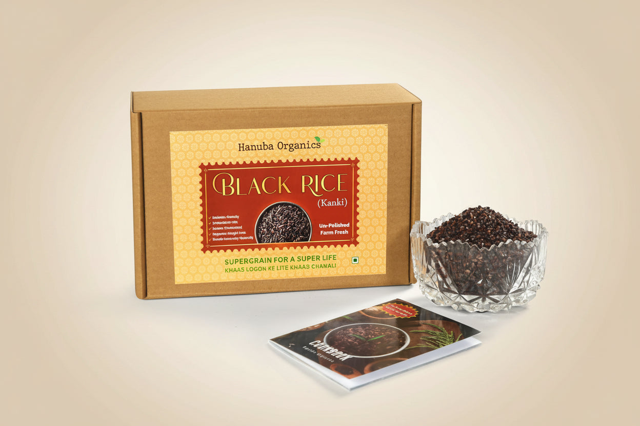 Hamuba Organics Black Rice (Kanki) product set featuring a brown cardboard box with a yellow label, a small clear glass bowl filled with black rice grains, and a small printed booklet on a white background.