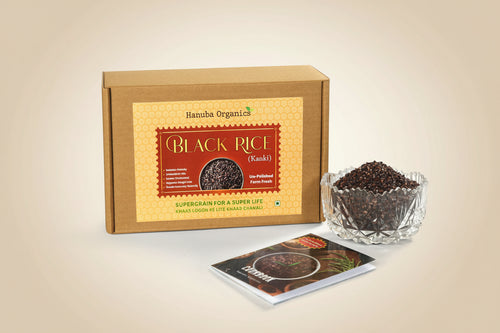 Hamuba Organics Black Rice (Kanki) product set featuring a brown cardboard box with a yellow label, a small clear glass bowl filled with black rice grains, and a small printed booklet on a white background.